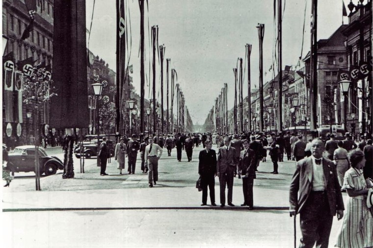 Schwarz-Weiß-Fotografie der Berliner Straße „Unter den Linden“. Links und rechts an Fahnenmasten und an den Häusern sieht man Hakenkreuz-Flaggen hängen.
