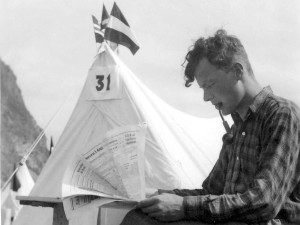 Schwarz-Weiß-Aufnahme von Willy Brandt, der mit Pfeife im Mund und eine Zeitung lesend vor einem Zelt sitzt.