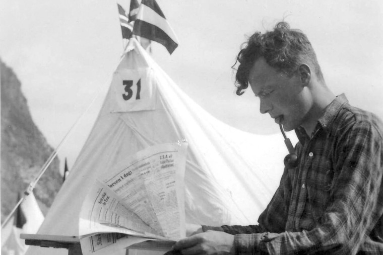 Schwarz-Weiß-Aufnahme von Willy Brandt, der mit Pfeife im Mund und eine Zeitung lesend vor einem Zelt sitzt.