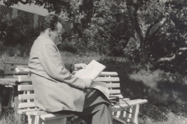 Schwarz-Weiß-Aufnahme von Willy Brandt, der im Garten auf einer Bank sitzt, Zigarette im Mund und eine Zeitung lesend.