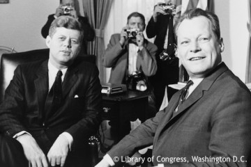 Willy Brandt sitzt neben US-Präsidenten John F. Kennedy im Weißen Haus. Fotografie in Schwarz-Weiß. Öffnet weitere Informationen zu den deutsch-amerikanischen Beziehungen.