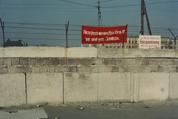Berliner Mauer, hinter der ein DDR-Banner zu sehen ist: „Nicht frech werden, Herr Brandt, wir sind gute Schützen.“. Daneben ist ein Plakat zu sehen auf dem steht: „Der Ruf der Wähler nach Entspannung wird sich durchsetzen!“.