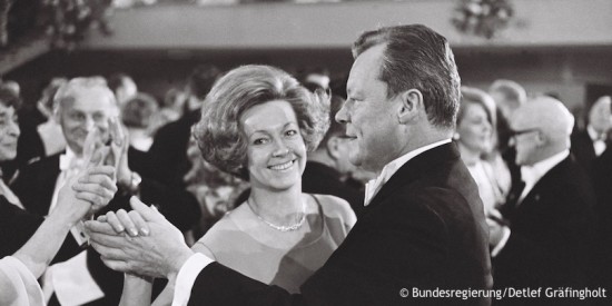 Willy Brandt tanzt mit Rut auf dem Bundespresseball. Sie schaut direkt in die Kamera, während man Brandt nur im Profil sieht. Im Hintergrund sind weitere tanzende Paare zu sehen. Fotografie in Schwarz-Weiß. Öffnet weitere Informationen zu dieser Ehe.