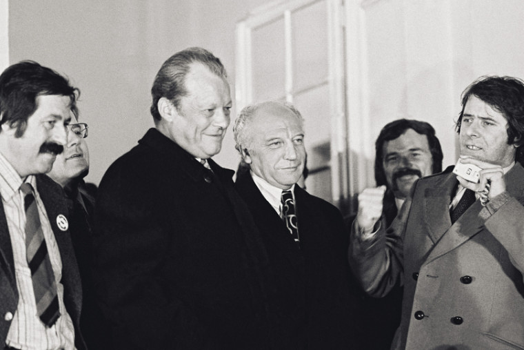 Willy Brandt steht zwischen Günter Grass und Walter Scheel. Schräg vor ihm spricht der Juso-Vorsitzende Wolfgang Roth. Fotografie in Schwarz-Weiß.