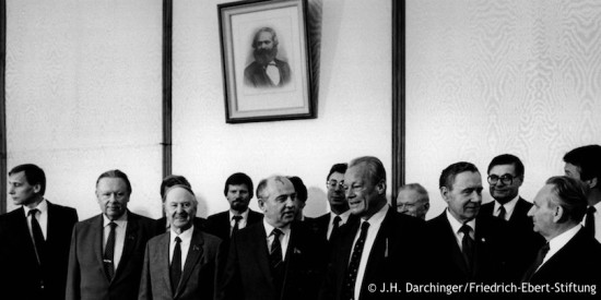 Gruppenbild von Willy Brandt und einer SPD-Delegation beim sowjetischen Generalsekretär Michail Gorbatschow. Im Hintergrund hängt ein Bild von Karl Marx. Fotografie in Schwarz-Weiß. Öffnet eine Auflistung der Reisen in den Jahren von 1983 bis 1992.