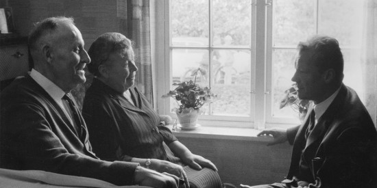 Willy Brandt sitzt bei einem Besuch in Lübeck seiner Mutter Martha Frahm und seinem Stiefvater Emil Kuhlmann gegenüber. Fotografie in Schwarz-Weiß. Öffnen, um mehr Informationen zu seiner Lübecker Familie zu erhalten.