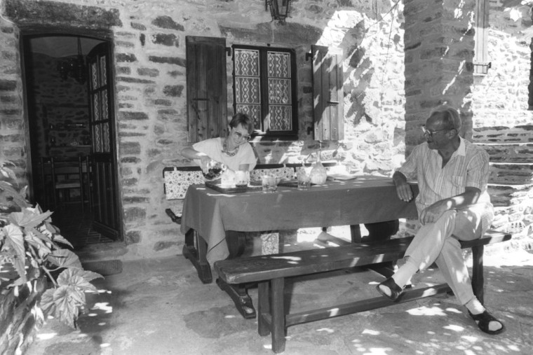 chwarz-Weiß-Aufnahme aus dem Jahr 1985 von Willy Brandt und seiner Frau Brigitte, die vor einem Ferienhaus in Gagnières (Frankreich) an einem Tisch sitzen. Brigitte Seebacher schenkt gerade etwas zu trinken ein.